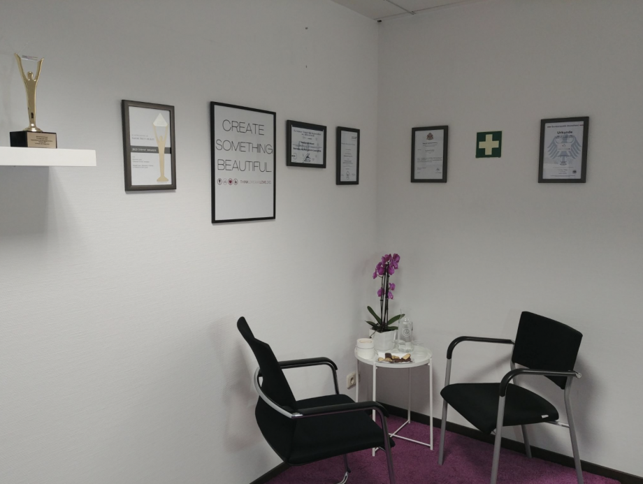 Büroraum mit Tisch und zwei Stühlen in der Ecke, an der Wand hängen verschiedene Zertifikate